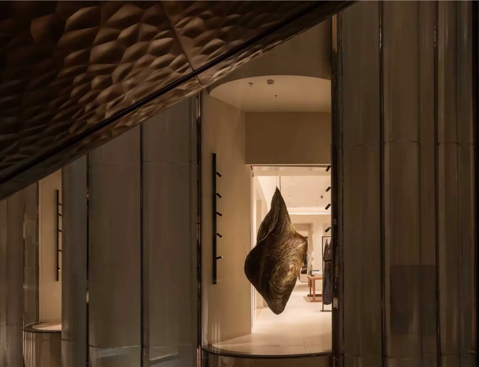Retail interior with fluted bronze panelling and a suspended sculptural form framing the entrance to the shop floor.