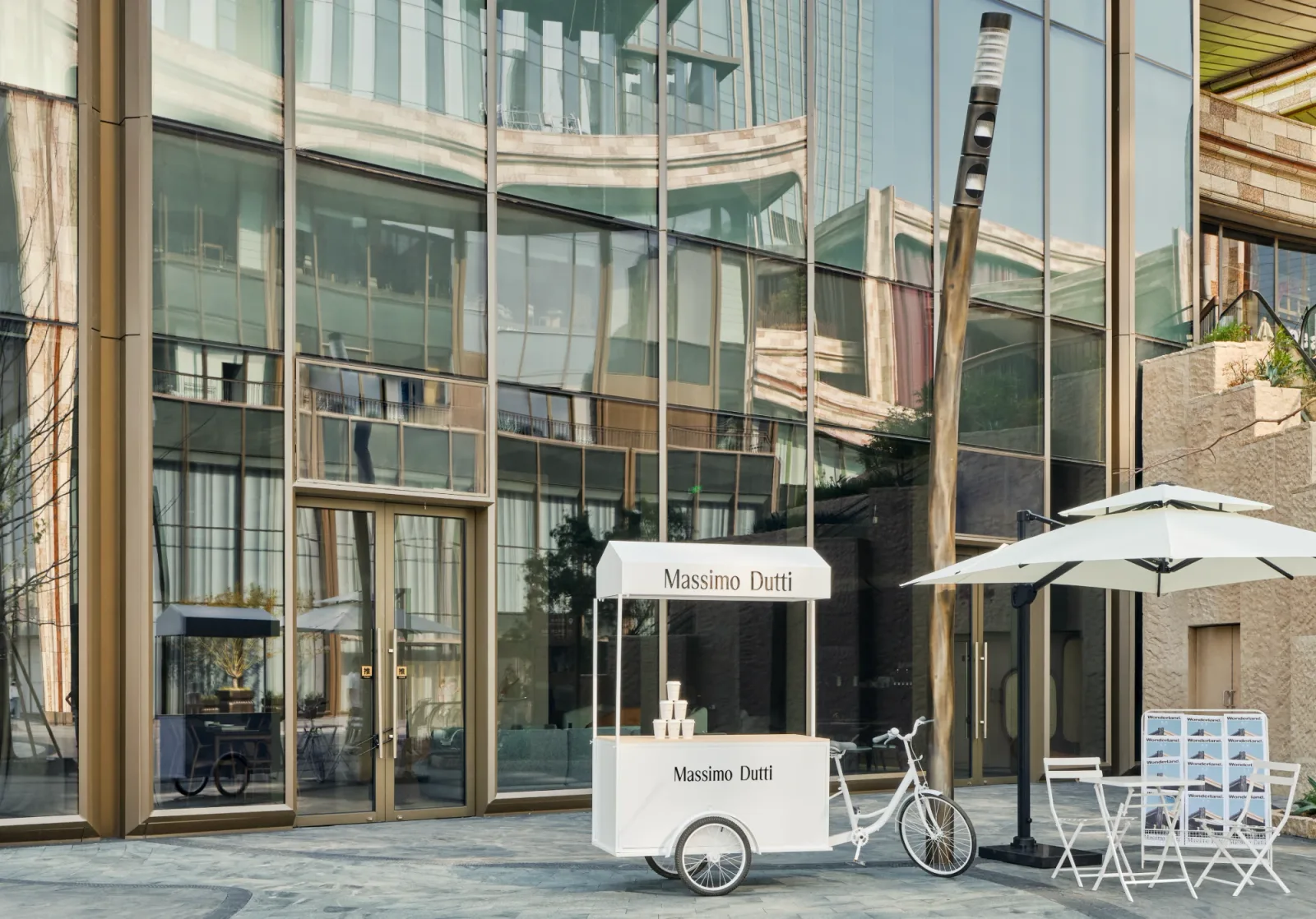Massimo Dutti branded service cart and parasol set outside a glazed retail façade.
