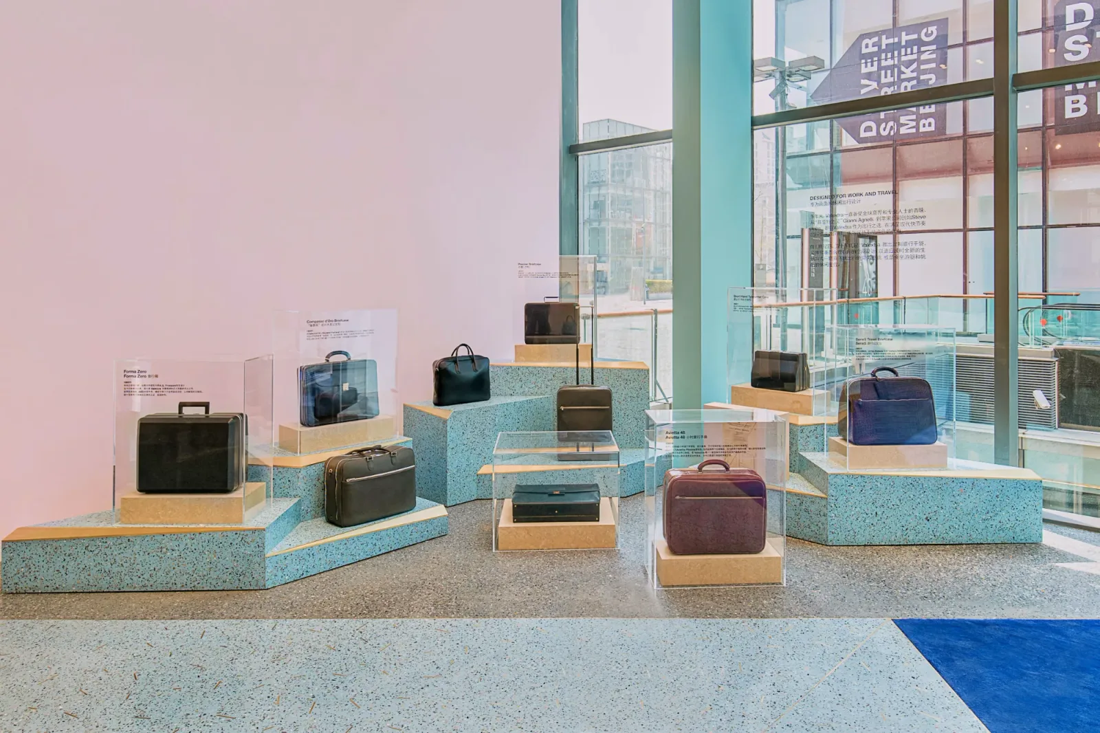 Valextra travel cases and briefcases displayed in vitrines on stepped blue terrazzo plinths.