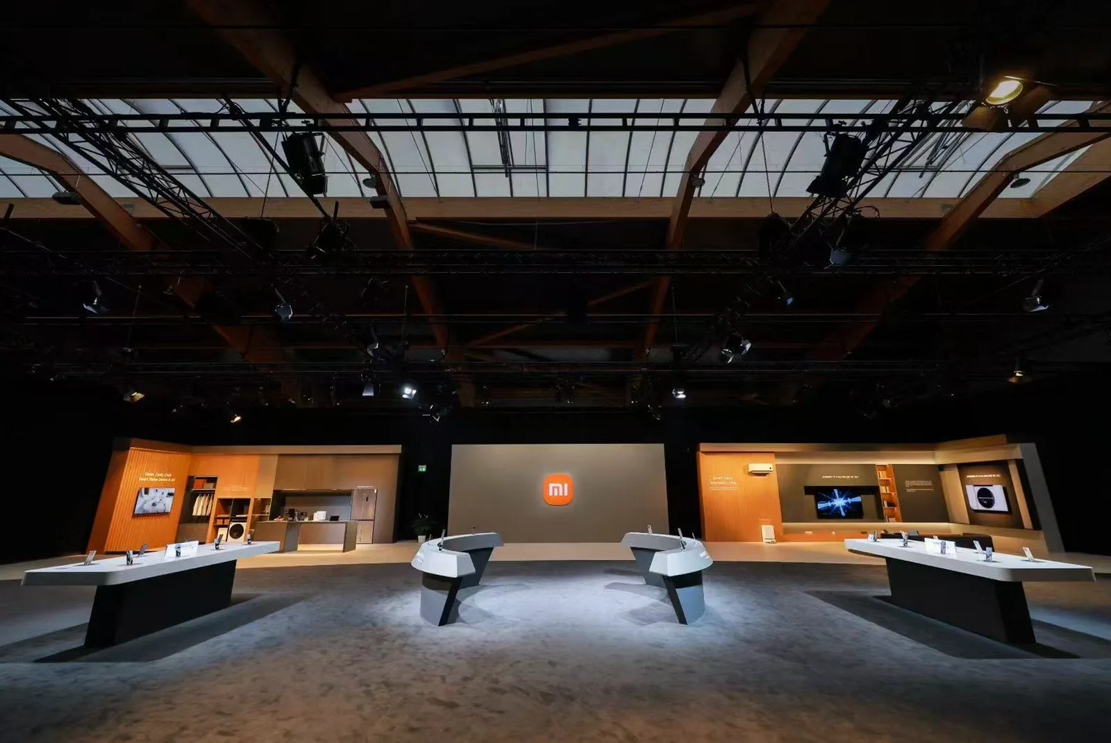 Xiaomi launch exhibition space with product display tables and an illuminated Mi logo on the rear wall.